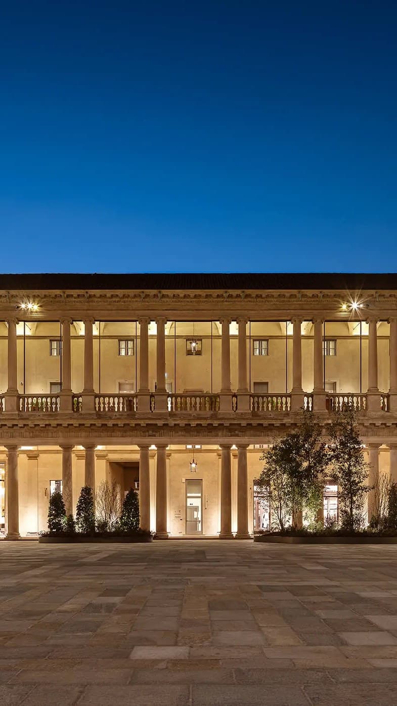 The colonnaded courtyard of a historic palazzo in central Milan, lit in the evening.