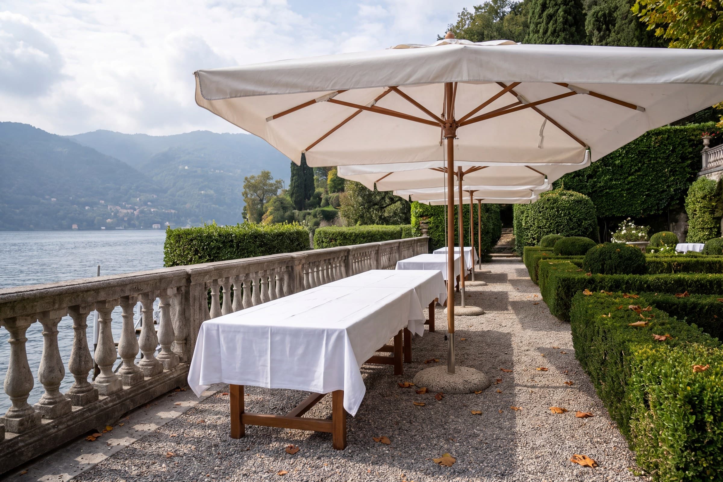 Il giardino di una villa sul lago con tavoli apparecchiati sotto gli ombrelloni.